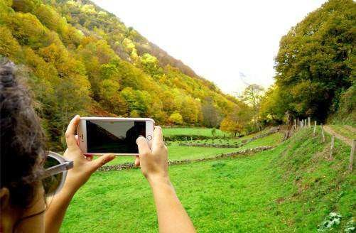 Una visitante fotografía un valle verde rodeado de bosque